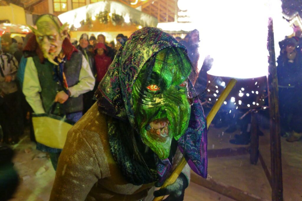 frau perchta with a green face and long pointy nose wearing a head scarf
