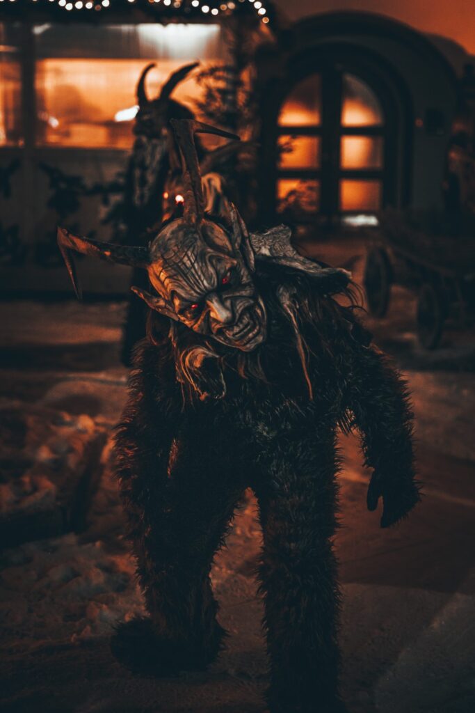 A Krampus Christmas Devil covered in fur with long horns stares at the camera with red hot eyes