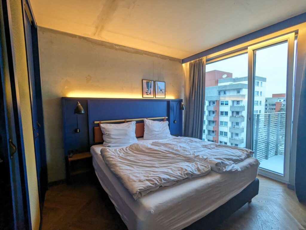 Berlin Aparthotel bed with white bedding, blue decor, gray walls overlooking the city