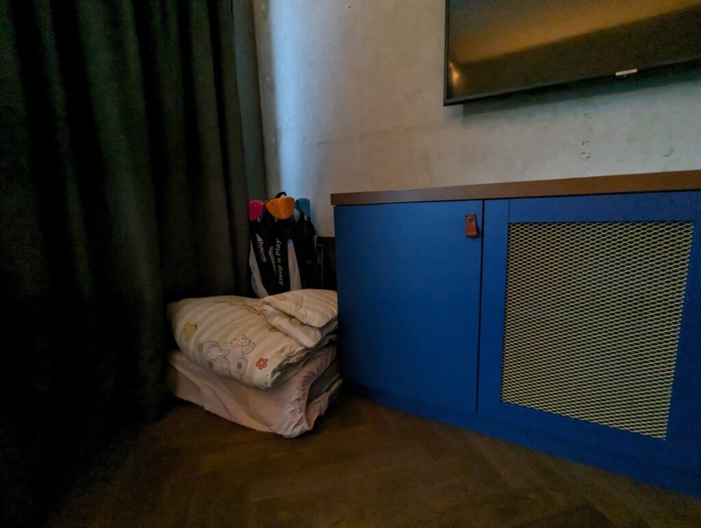 Traveling with a baby to Germany means needing a travel crib. Baby Travel Crib and bedding/linens folded up in the corner of Berlin Aparthotel with blue cabinet next to it