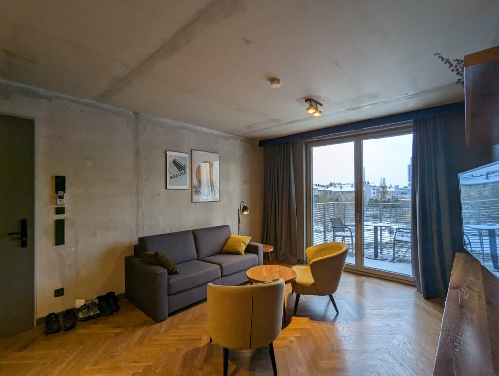 Berlin Mitte Apartment Hotel family room with grey walls, yellow pillows, 2 chairs, wooden floor, and overlooking the city