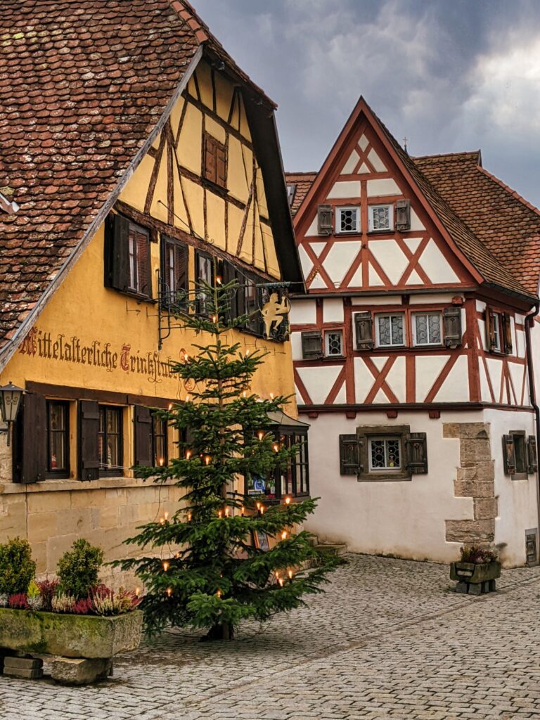 rothenburg ob der tauber at christmas with a christmas tree on the cobblestone street in front of a yellow fachwerkhaus