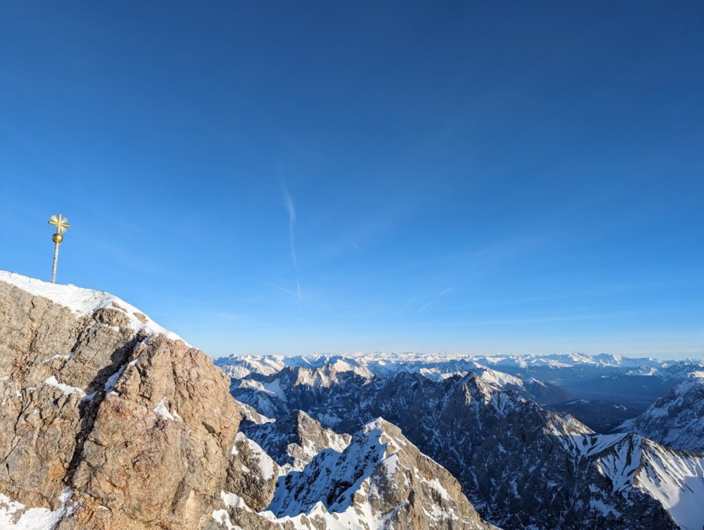 golden cross on top of the zugspitze, the tallest mountain in germany with the Bavarian Alps in the distance